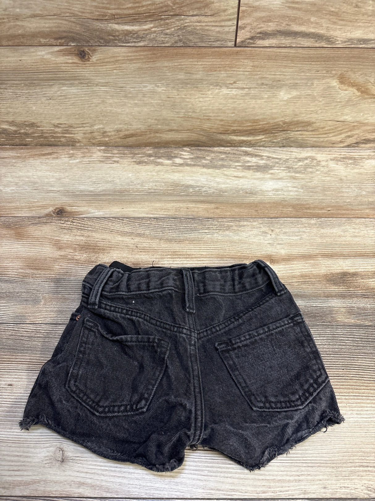 Back view of toddler black Old Navy high-rise distressed denim shorts showing frayed hem and back pockets on wood backdrop
