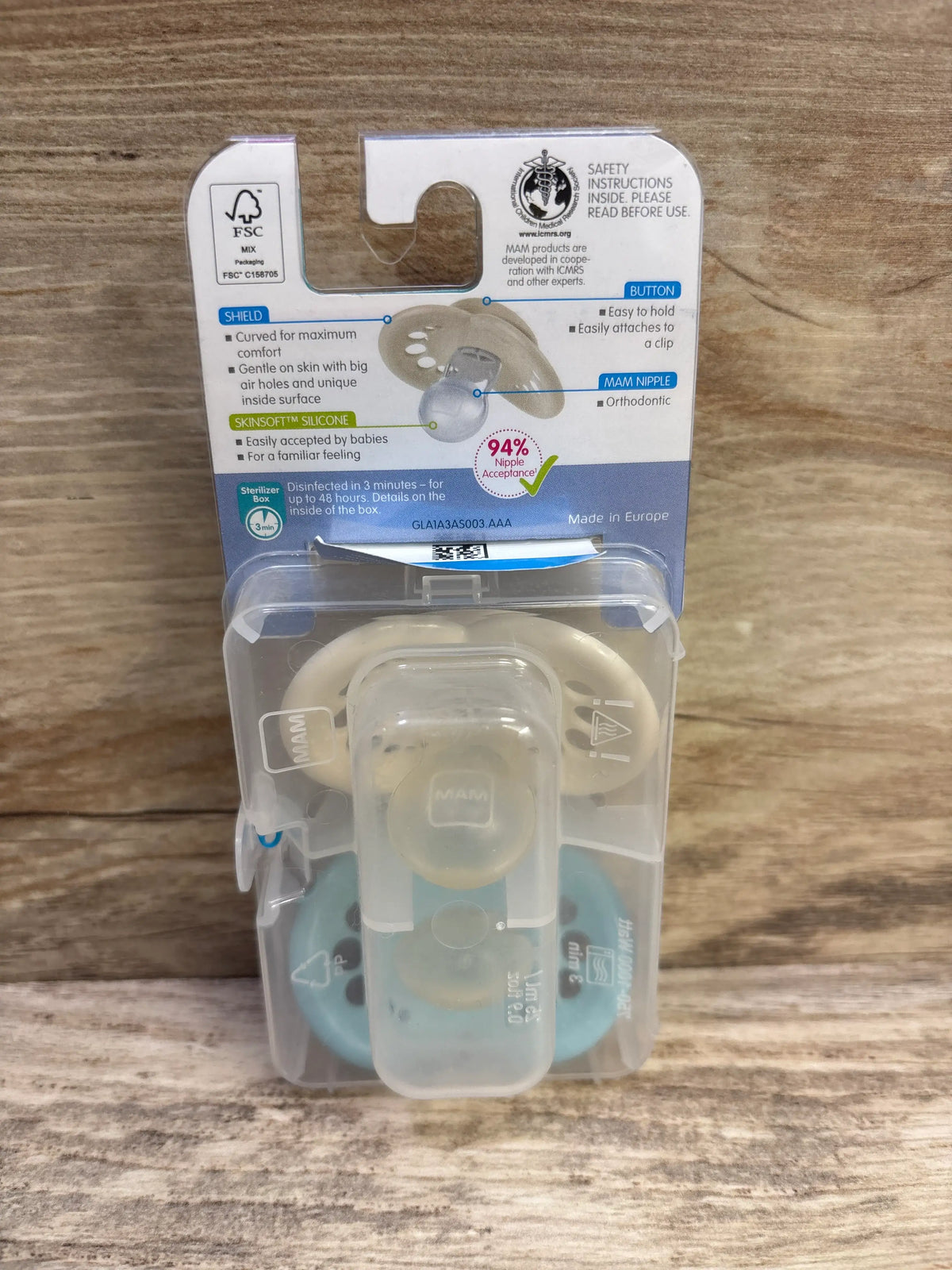 Front view of two MAM Original pacifiers in teal and cream packaging with curved shields and silicone nipples on wood