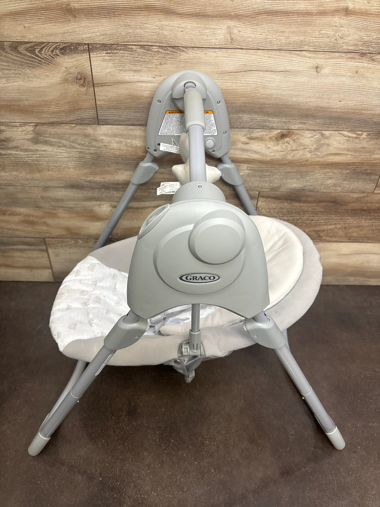 Top view of Graco Slim Spaces compact baby swing showing gray motor housing with Graco logo and light-gray padded seat against wood backdrop