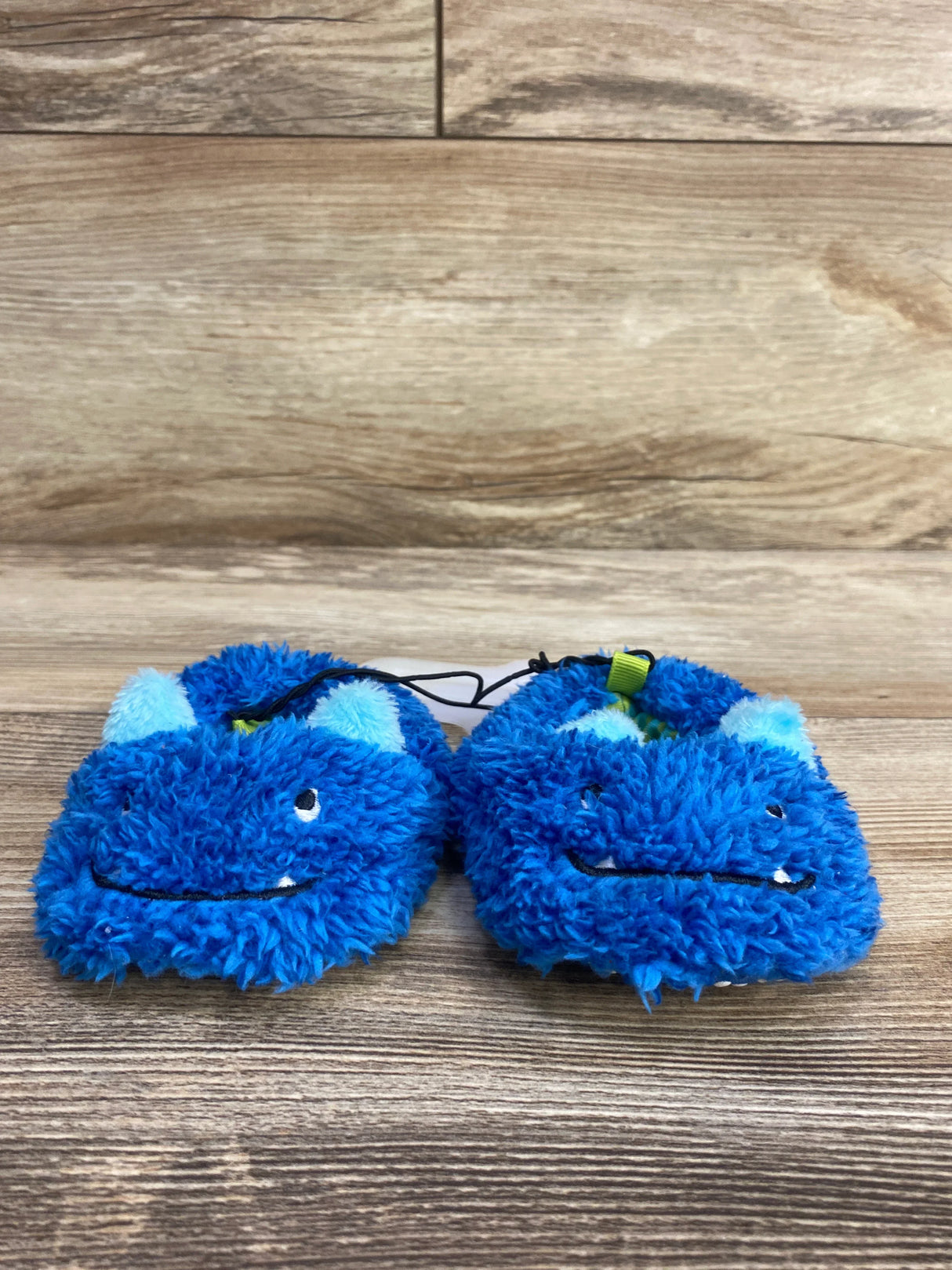 Pair of fluffy blue baby slippers with monster faces and ears on wooden floor