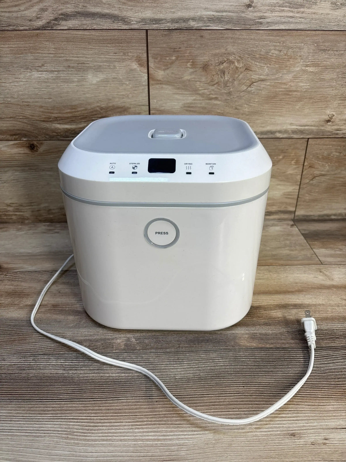 White baby bottle sterilizer with lid and power cord on wood floor background