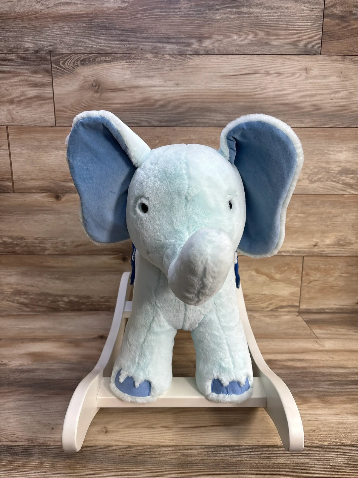 Front view of Lilly Pulitzer x Pottery Barn Kids elephant nursery rocker showing light blue plush elephant with large ears on white wooden rocker against wood-plank background