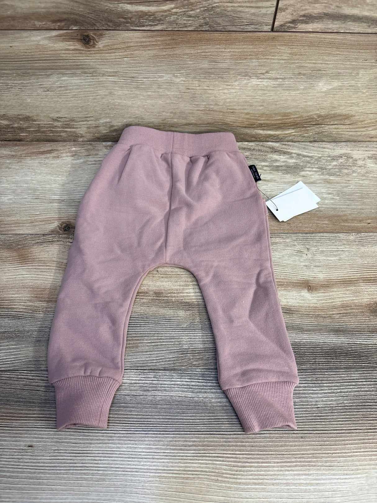 Flat lay of NEW Tiny Tribe sweat pants in dusty lilac showcasing ribbed cuffs and waistband with hangtag on wood plank floor