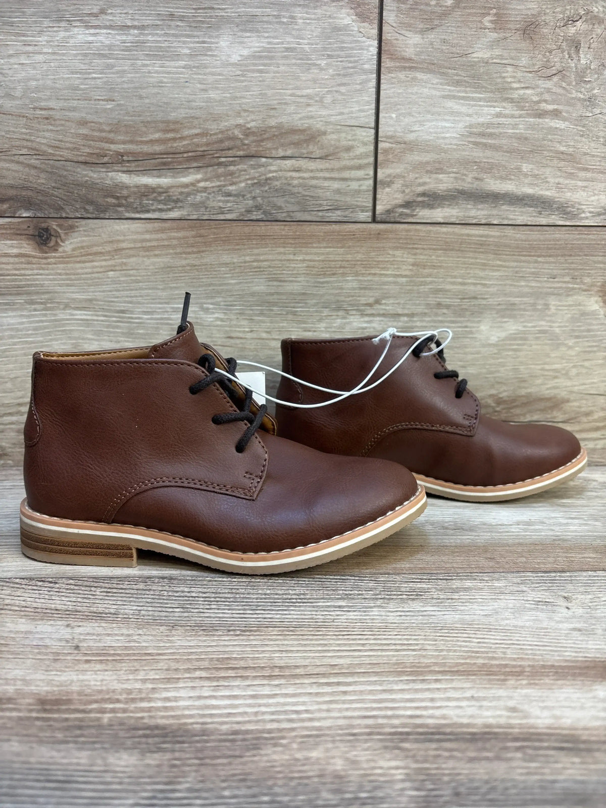Front and side view of Cat & Jack Filip boots showcasing brown uppers, black lace-up closure, and tan soles on a wood floor