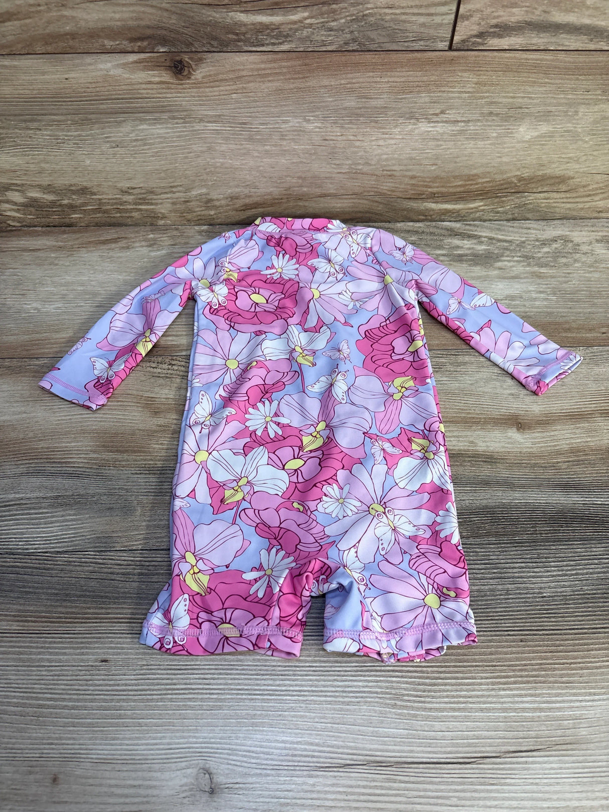 Back view of UMELOK floral rashguard romper, long sleeves and ruffle leg openings, laid flat on wood