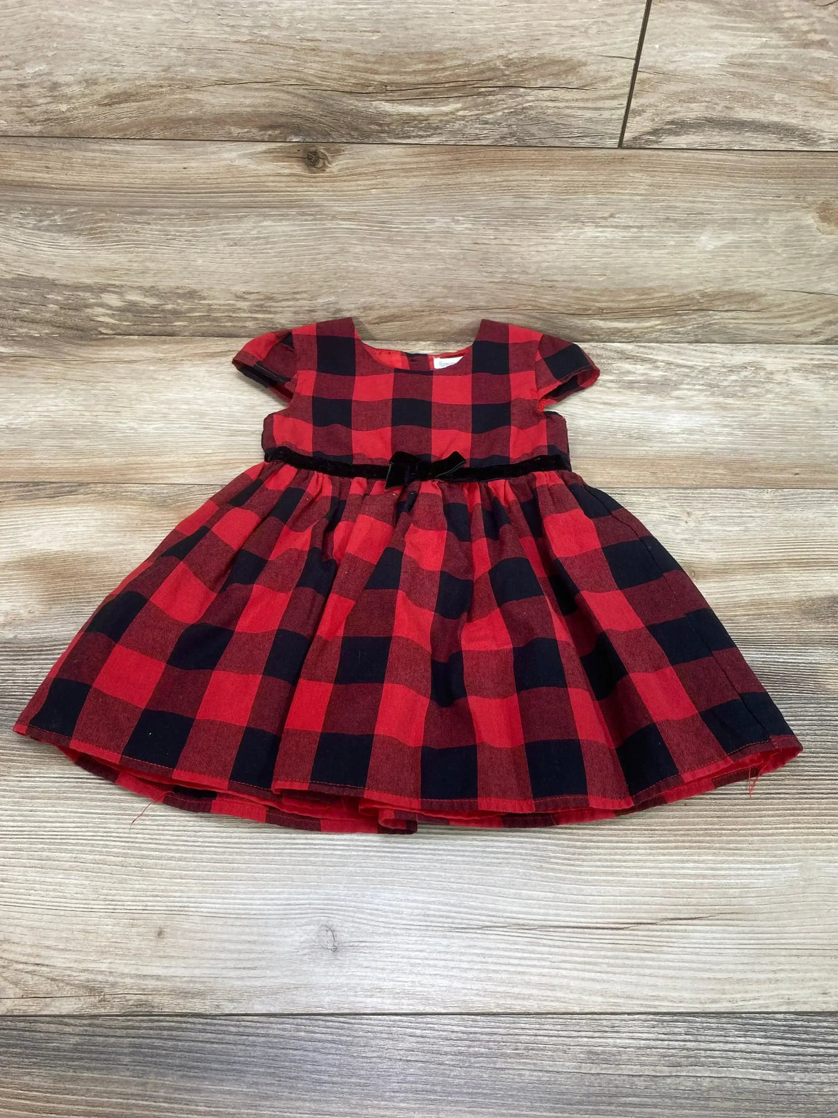 Front view of Forever Me Buffalo Check Cap Sleeve Dress in red size 2T showcasing red and black plaid dress with velvet bow waist on wood plank backdrop