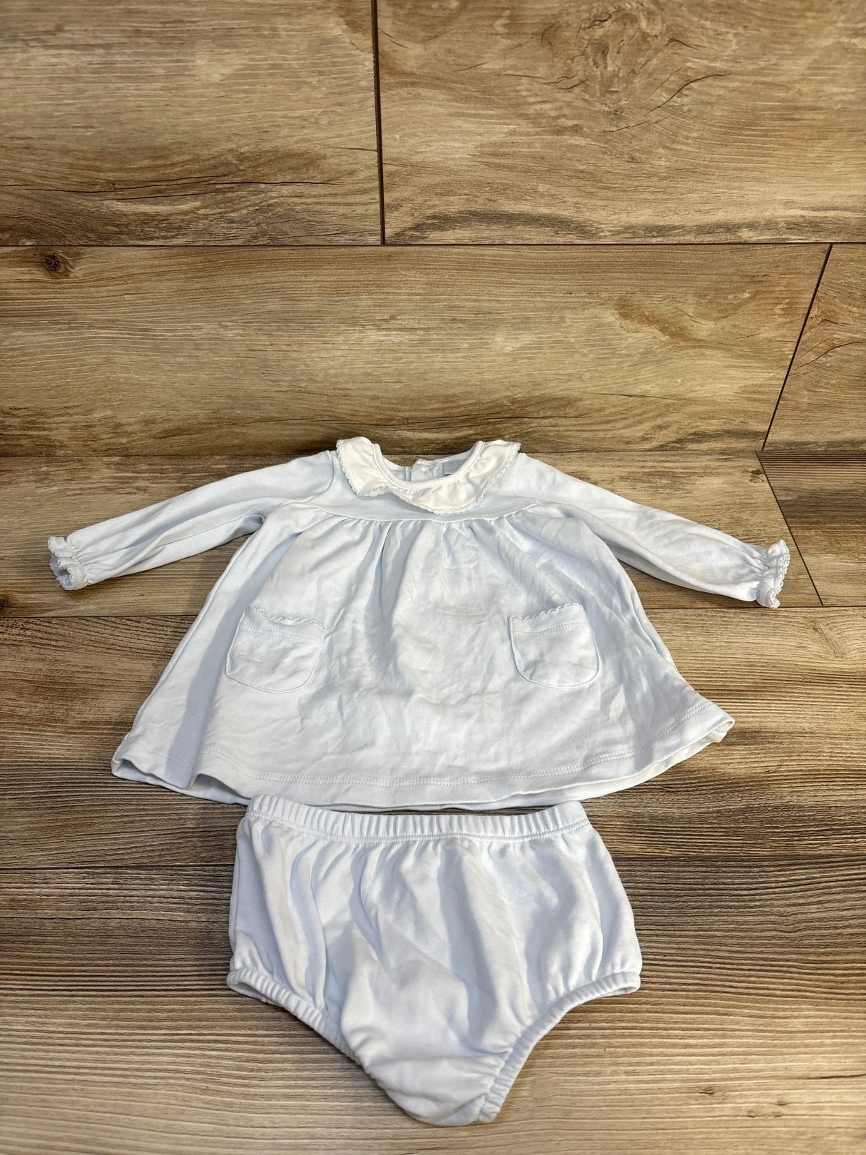 Front view of baby-blue Edgehill long-sleeve dress and bloomers showing ruffled collar and pockets on wooden floor