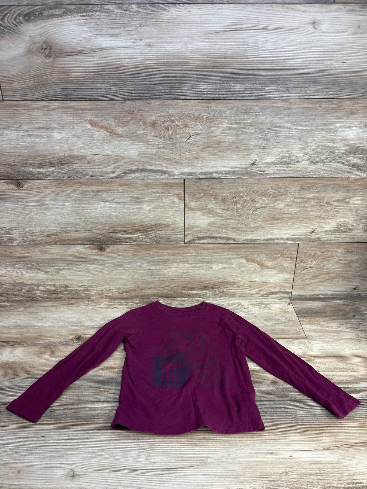 Burgundy long sleeve kids shirt with graphic print on wood floor background