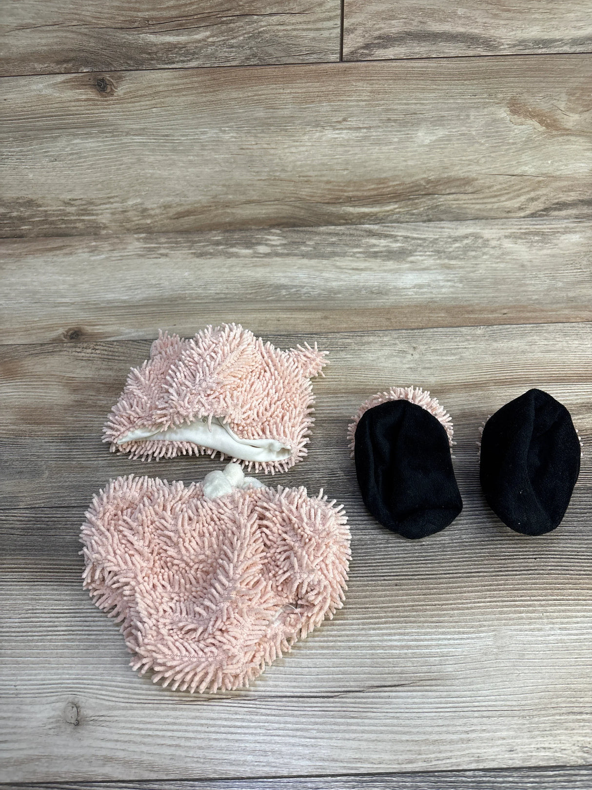 Soft pink and black chenille baby booties on wood floor, cozy infant footwear for newborns and toddlers