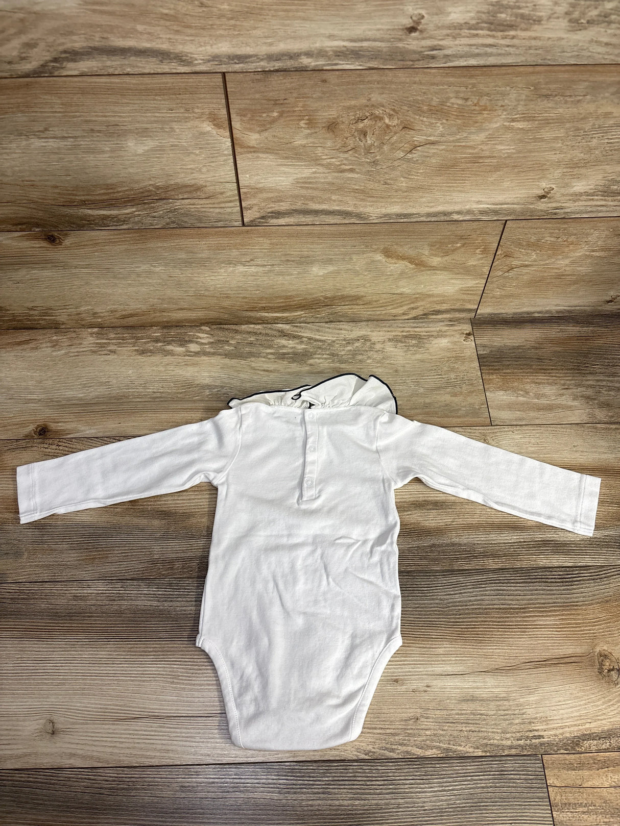 White long-sleeve baby bodysuit with ruffled collar on wooden floor