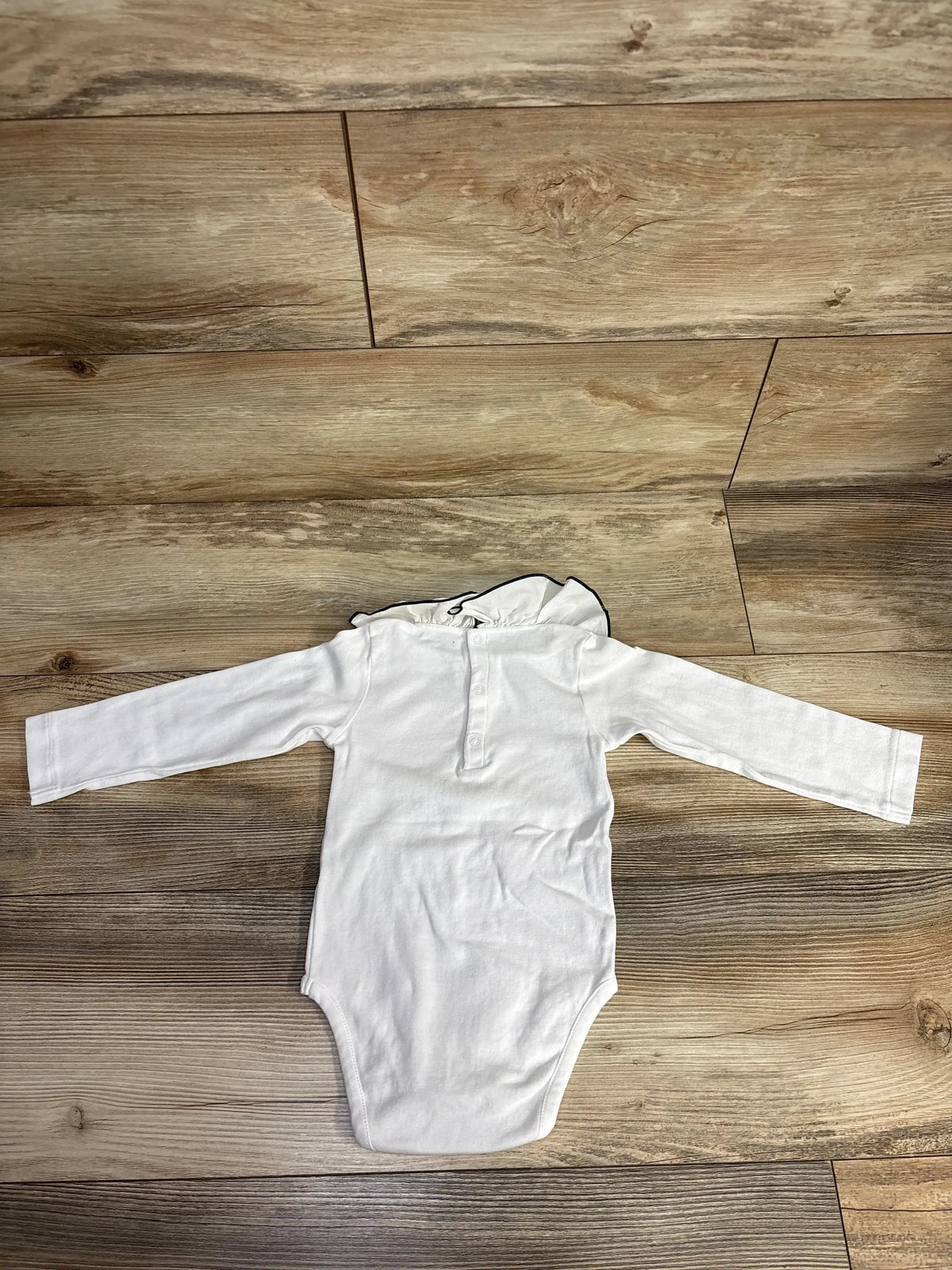 White long-sleeve baby bodysuit with ruffled collar on wooden floor