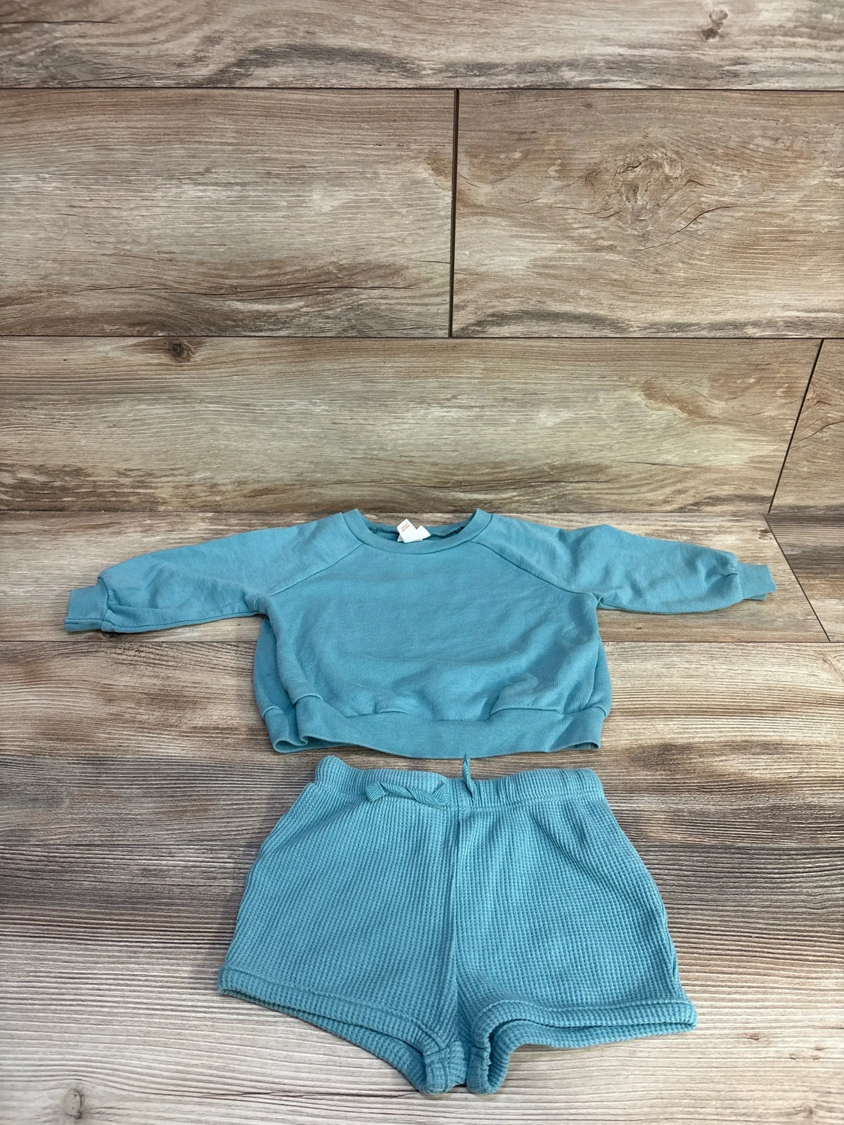 Flat lay of teal baby long-sleeve shirt and waffle-knit shorts showing waffle texture and drawstring waist on wood background