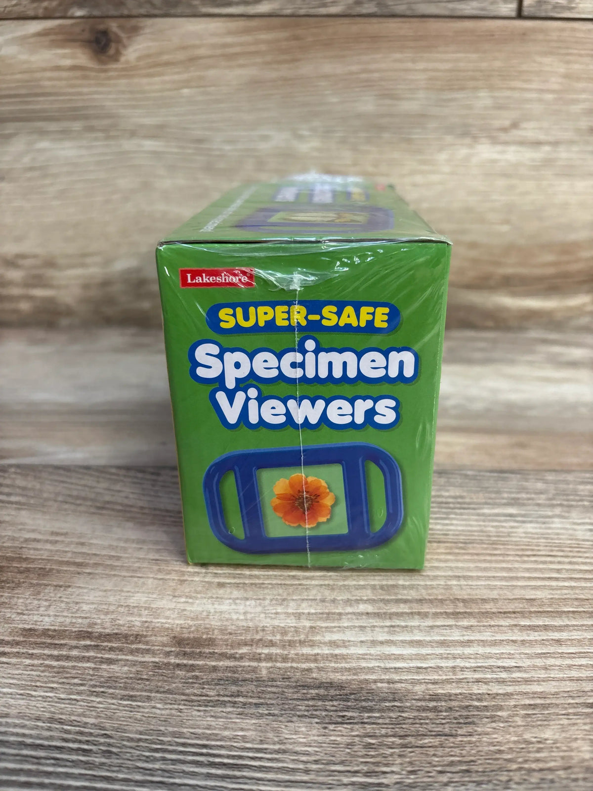 Front view of Lakeshore Super-Safe Specimen Viewers box showing product title and blue viewer illustration on a wood tabletop