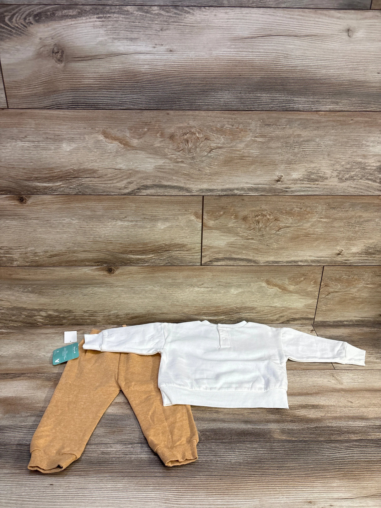 Flat lay of Disney Baby Winnie the Pooh 2-piece set showing white sweatshirt back and tan joggers on wood background