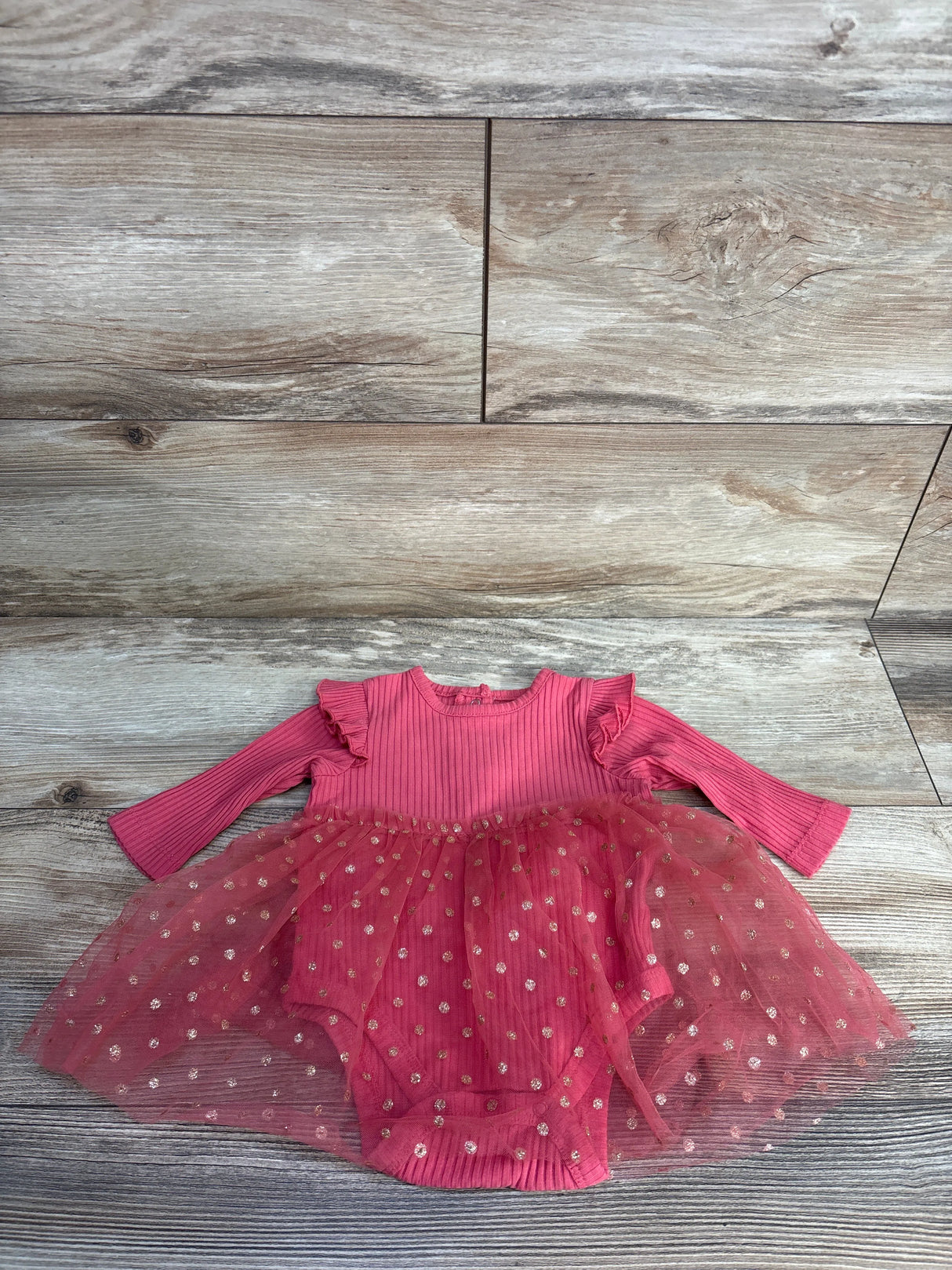 Pink baby girl dress with ruffled long sleeves and dotted tulle skirt on wood floor