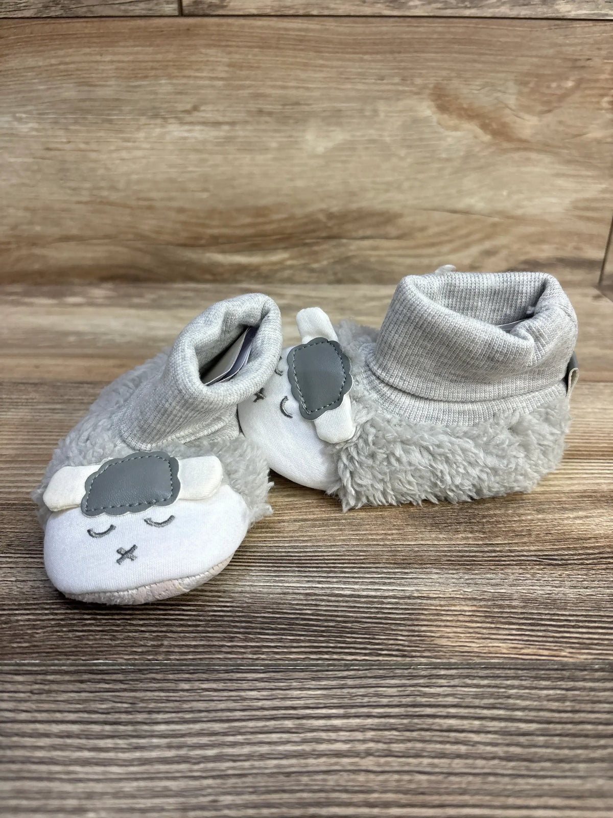 Gray baby booties with sheep faces and soft textured fabric on wooden surface