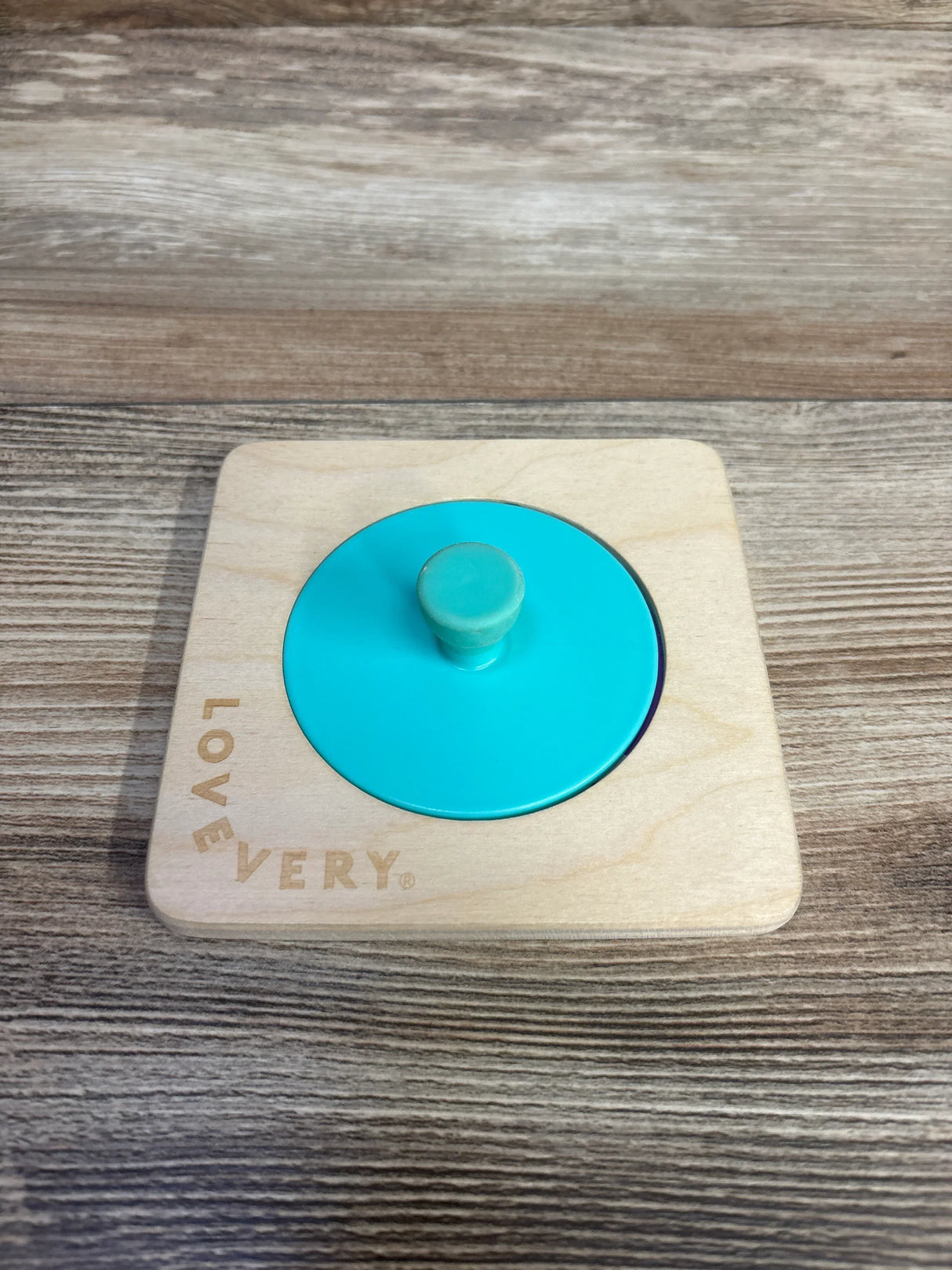 Lovevery wooden circle puzzle with turquoise knob on wood background