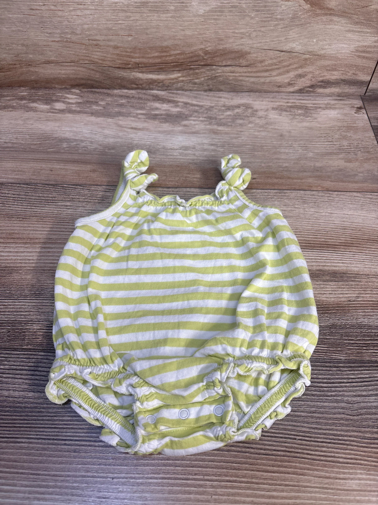 Top-down view of Old Navy green and white striped bubble romper with knotted shoulder straps, elastic leg openings and snap crotch on wood background