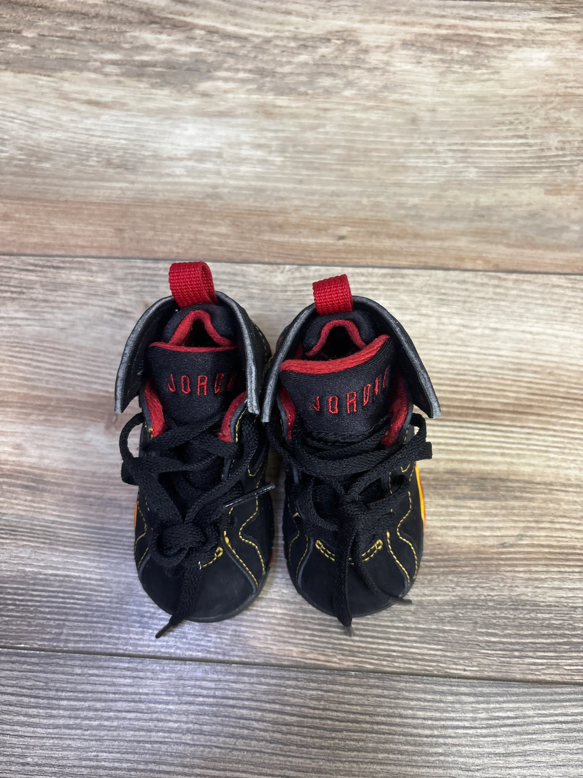 Top view of Air Jordan 7 Retro TD Citrus sneakers showcasing black uppers with red and yellow accents on a wood surface