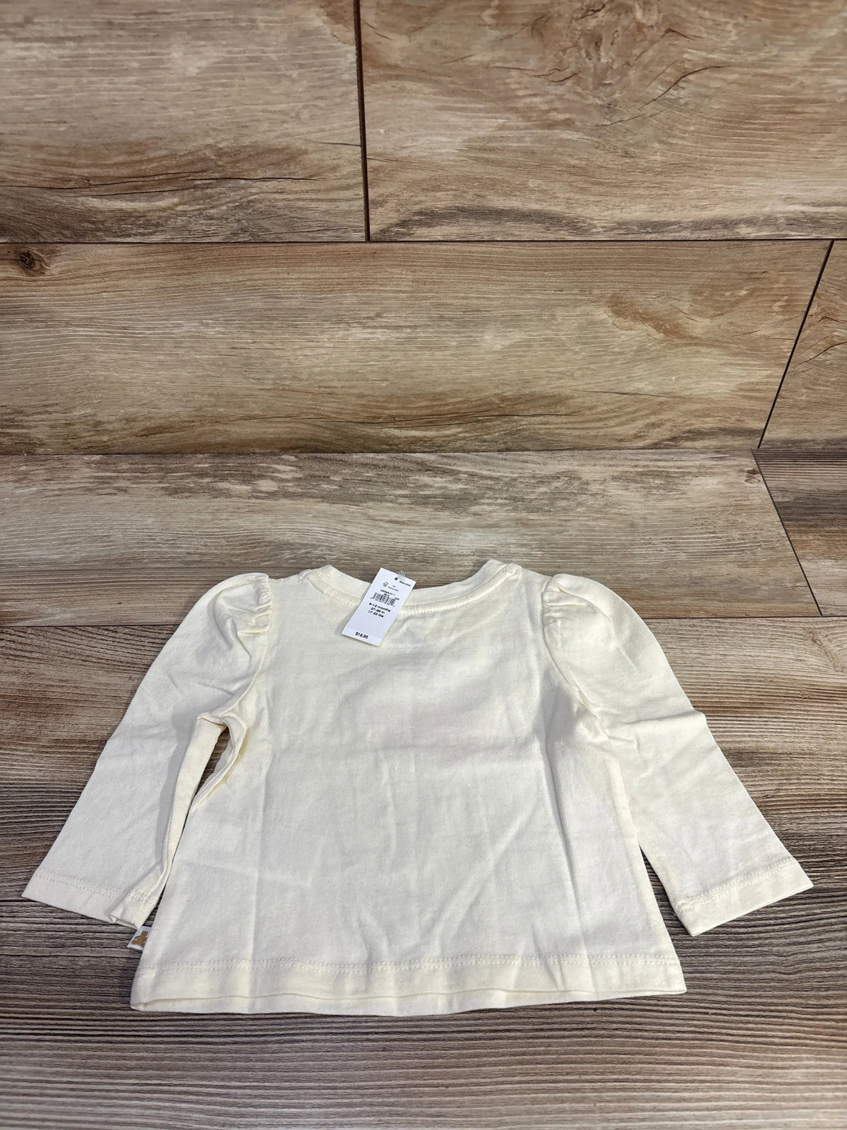 Front view of Baby Gap cream long puff sleeve shirt showcasing puffed shoulders and long sleeves on a wood floor
