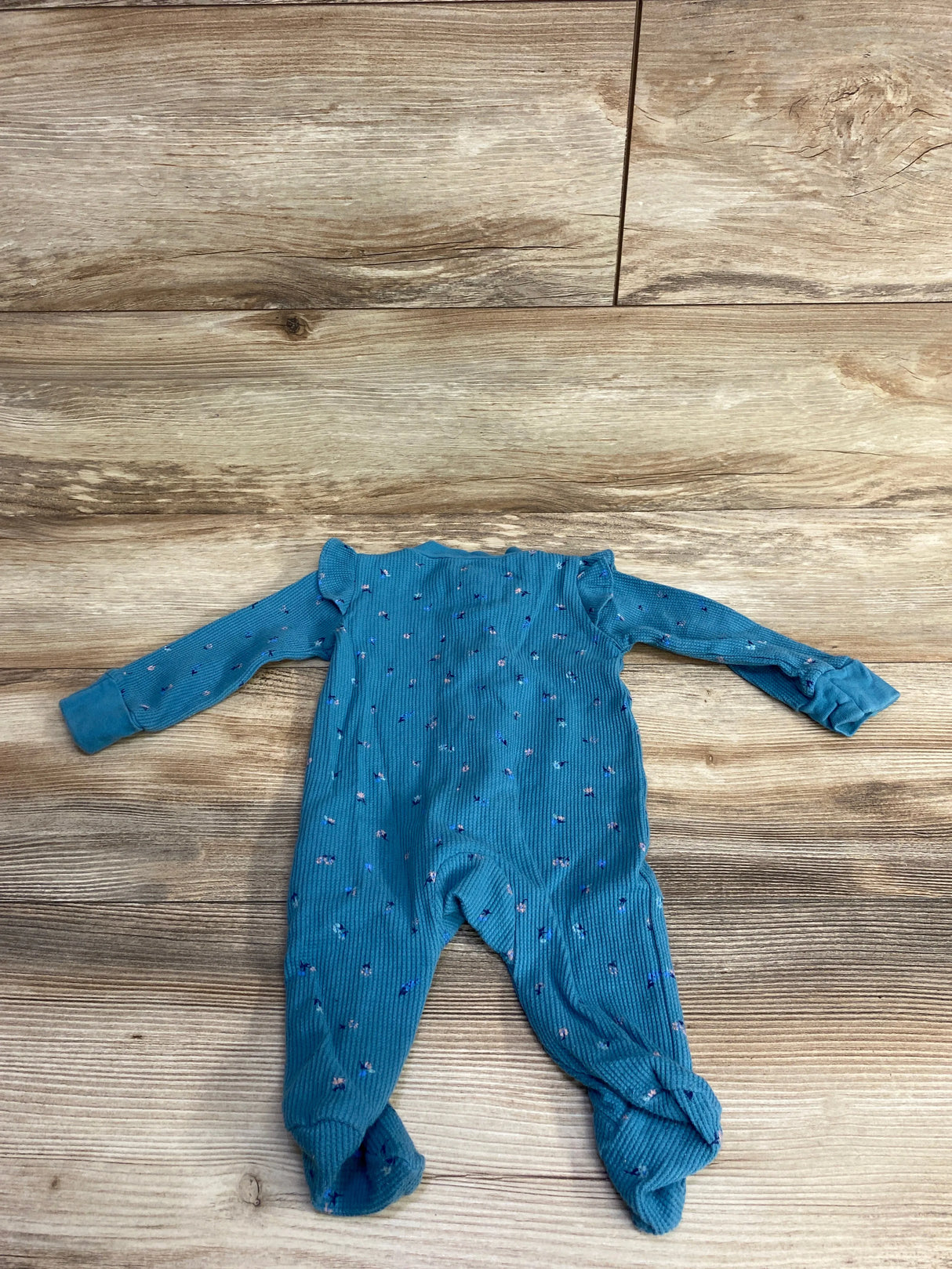 Blue long-sleeve baby onesie with small floral print laid flat on wooden floor