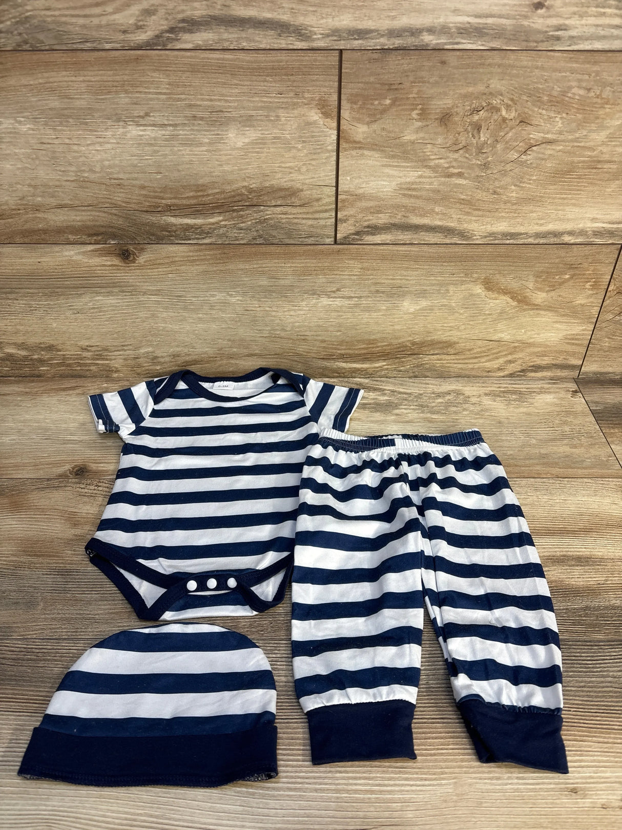 Striped baby outfit set with onesie, pants, and hat in navy blue and white on wood background