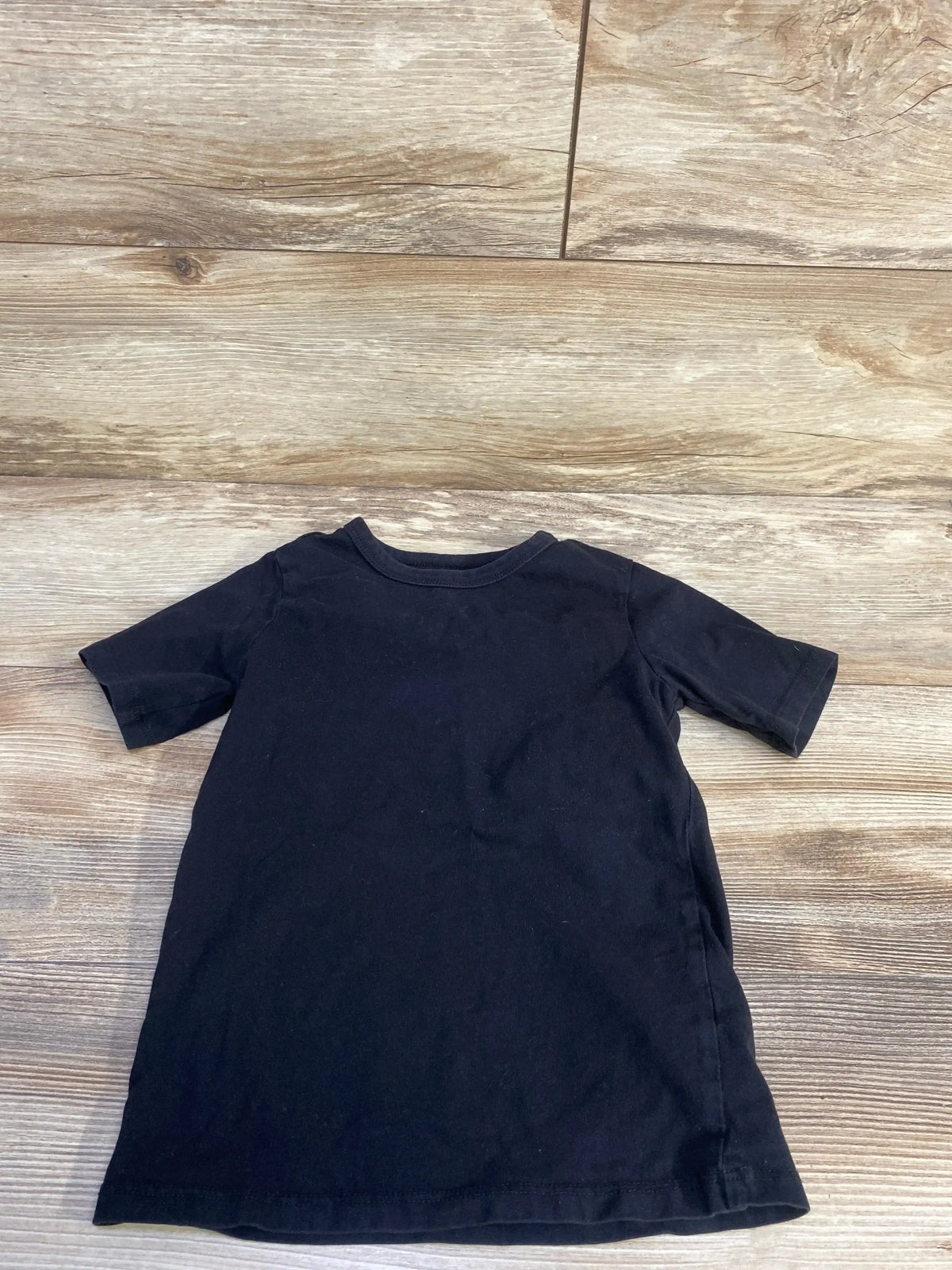 Flat lay of Children’s Place black short-sleeve toddler T-shirt size 5T showing front on wood plank floor