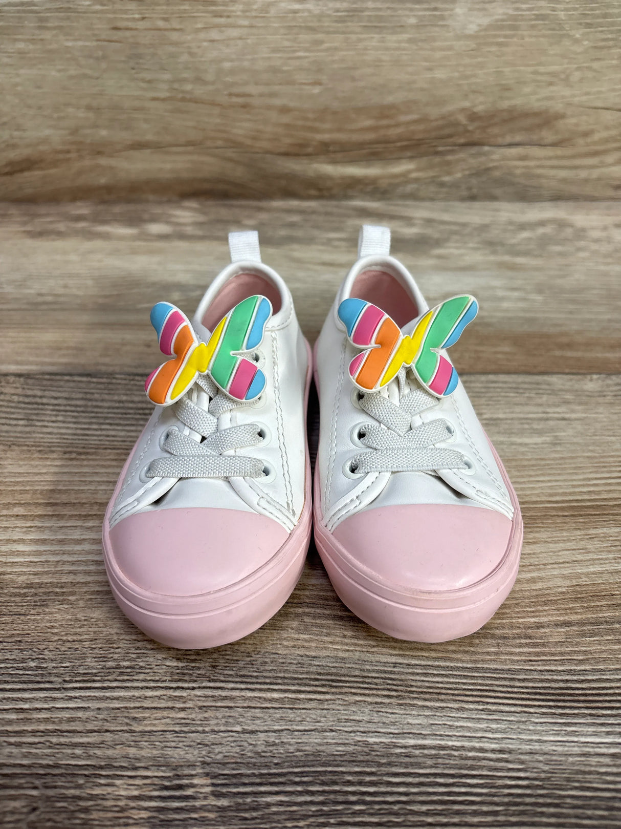 Pair of white and pink sneakers with colorful rainbow butterfly clips on wooden floor