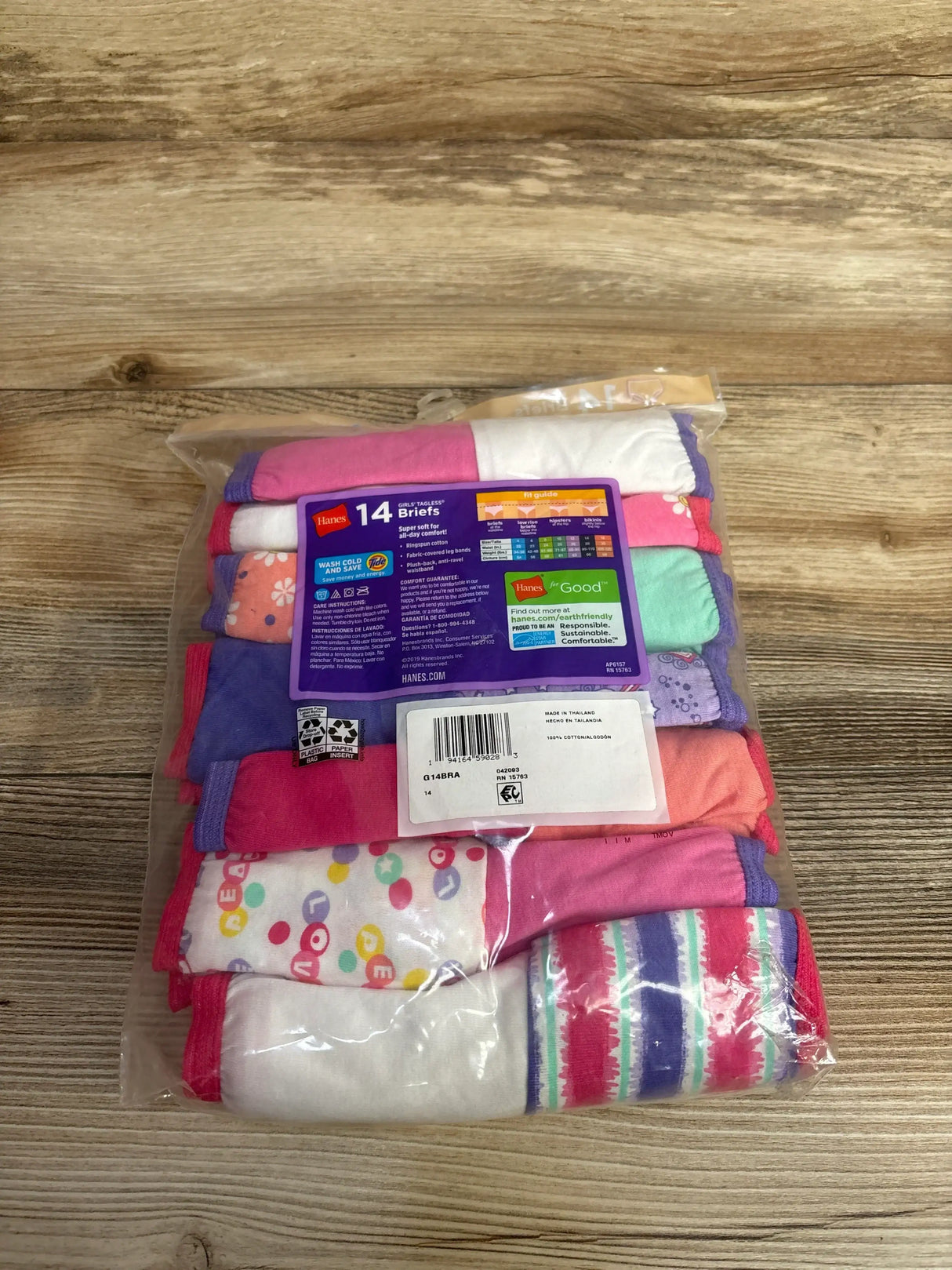 Top-down view of Hanes girls' 14-pack tagless cotton briefs showcasing assorted colorful patterns and solids on wood
