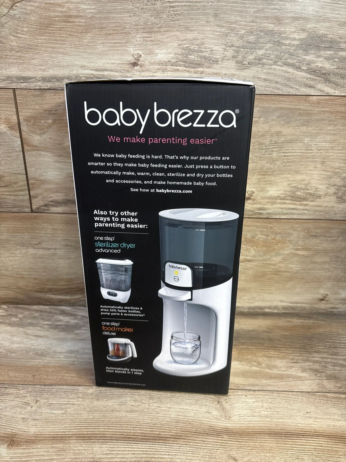 Front view of Baby Brezza Instant Baby Bottle Warmer box showing babybrezza logo and dispenser spout with wood plank background