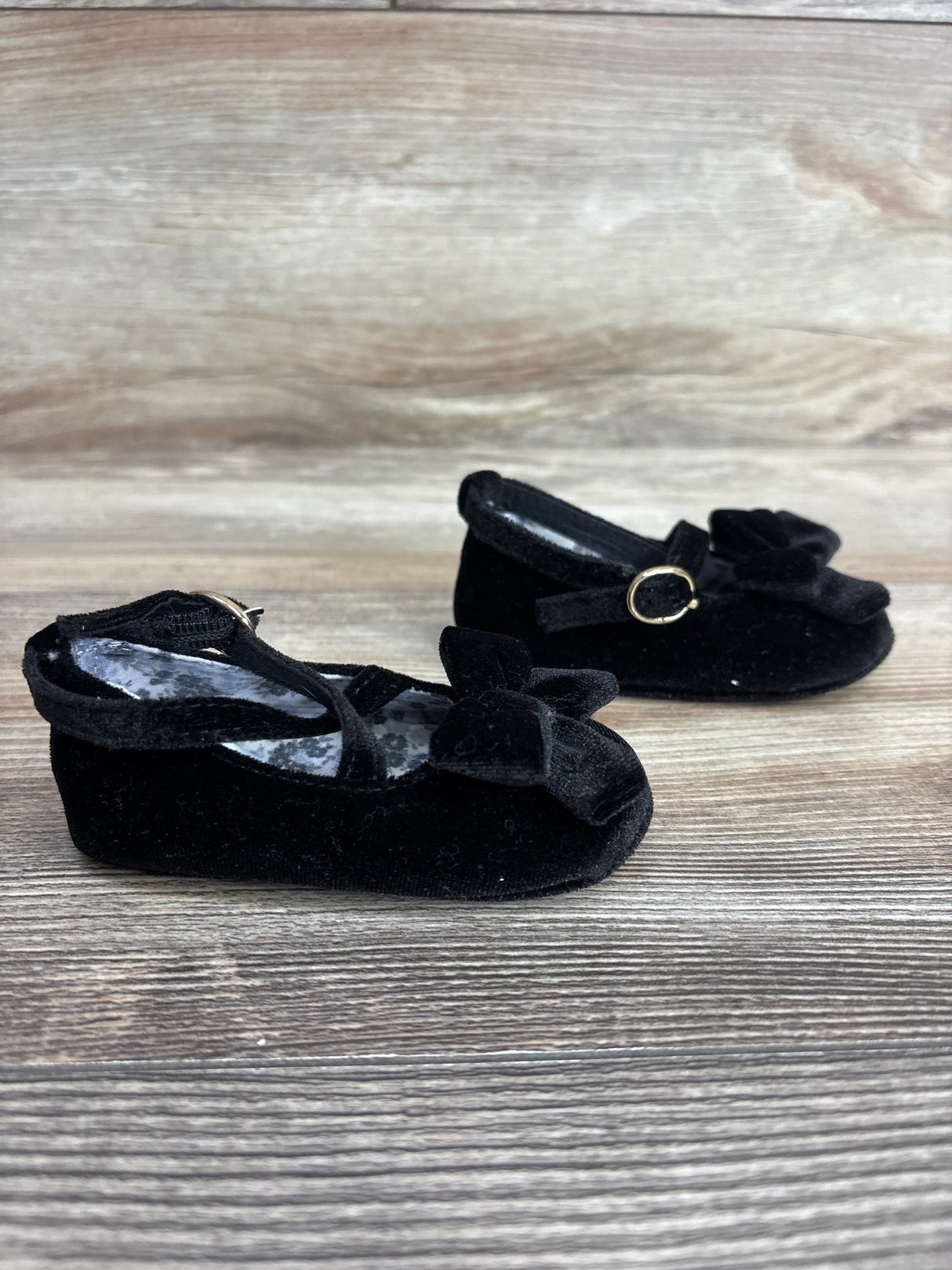 Black velvet baby shoes with bows and ankle straps on wooden background