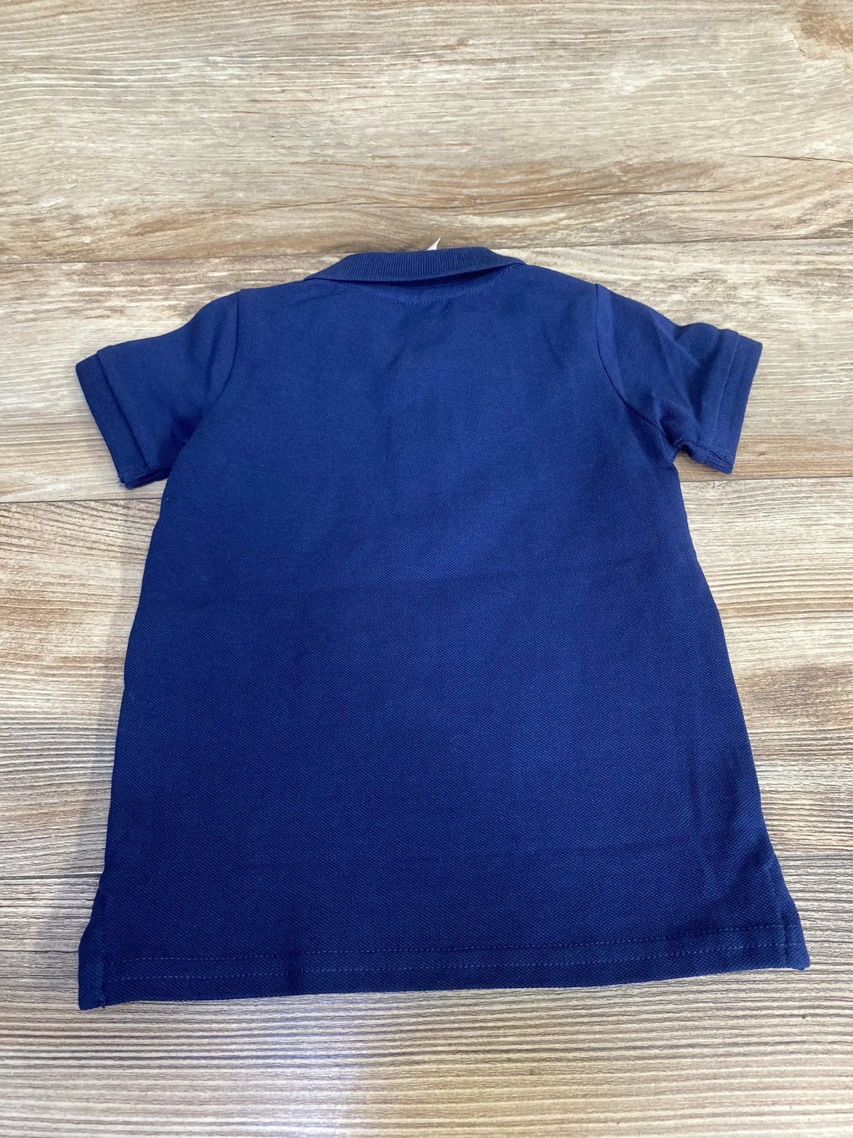 Back view of navy H&M baby polo shirt (12 months) showing short sleeves and ribbed collar laid flat on light wood surface