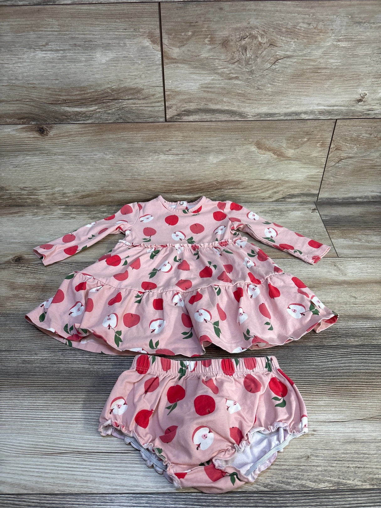 Pink baby dress and bloomers set with red apple print on wood background