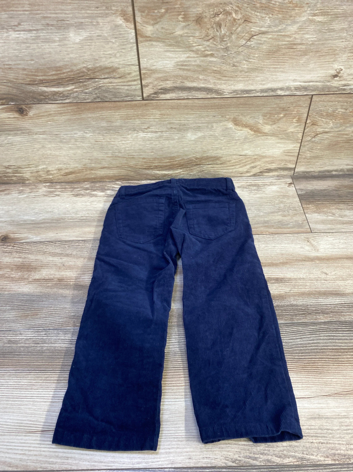 Back view flat lay of Janie & Jack navy corduroy toddler pants showing straight legs and back patch pockets on wood floor