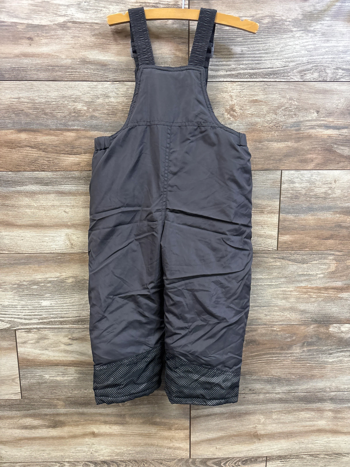 Front view of grey toddler snow bib with elastic shoulder straps and reinforced dotted cuffs on wooden hanger