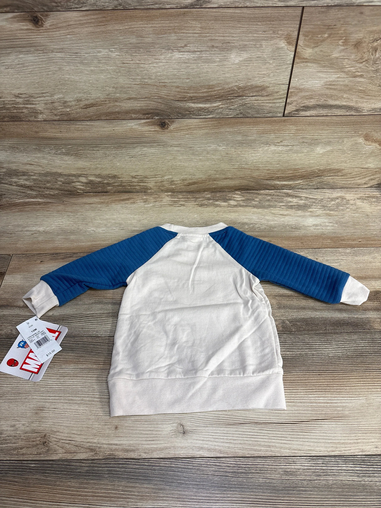 Cream long sleeve baby shirt with blue ribbed sleeves, laid flat on wood floor