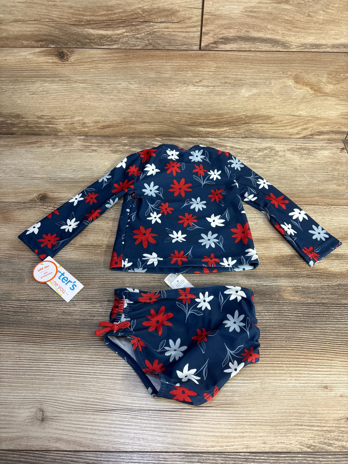 Top view of navy floral two piece rash guard swimsuit with long sleeves and bikini bottoms on a wood background