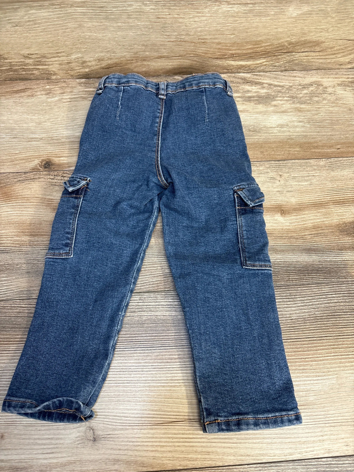 Kids denim cargo pants with side pockets, laid flat on wood floor