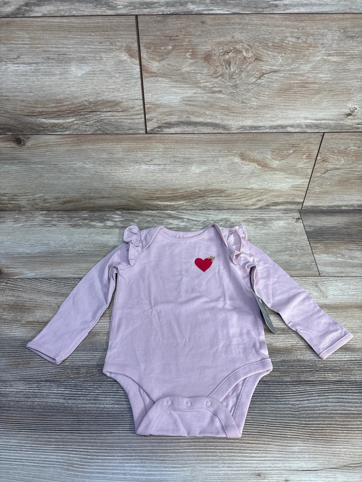 Front view of pink Baby Gap bodysuit with long sleeves, ruffled shoulders and heart motif on wood-grain background