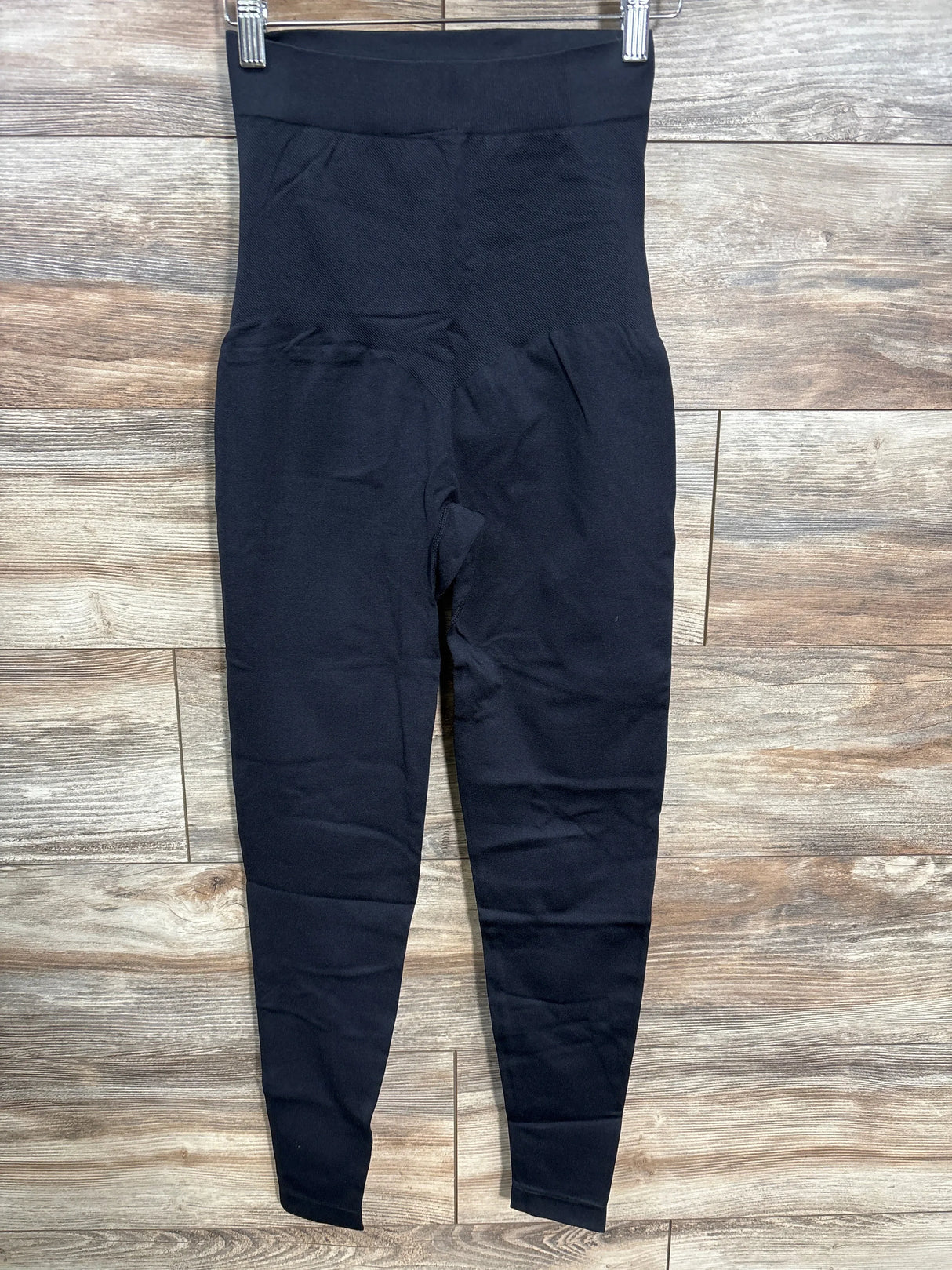 Black high-waisted maternity leggings on hanger against wood background