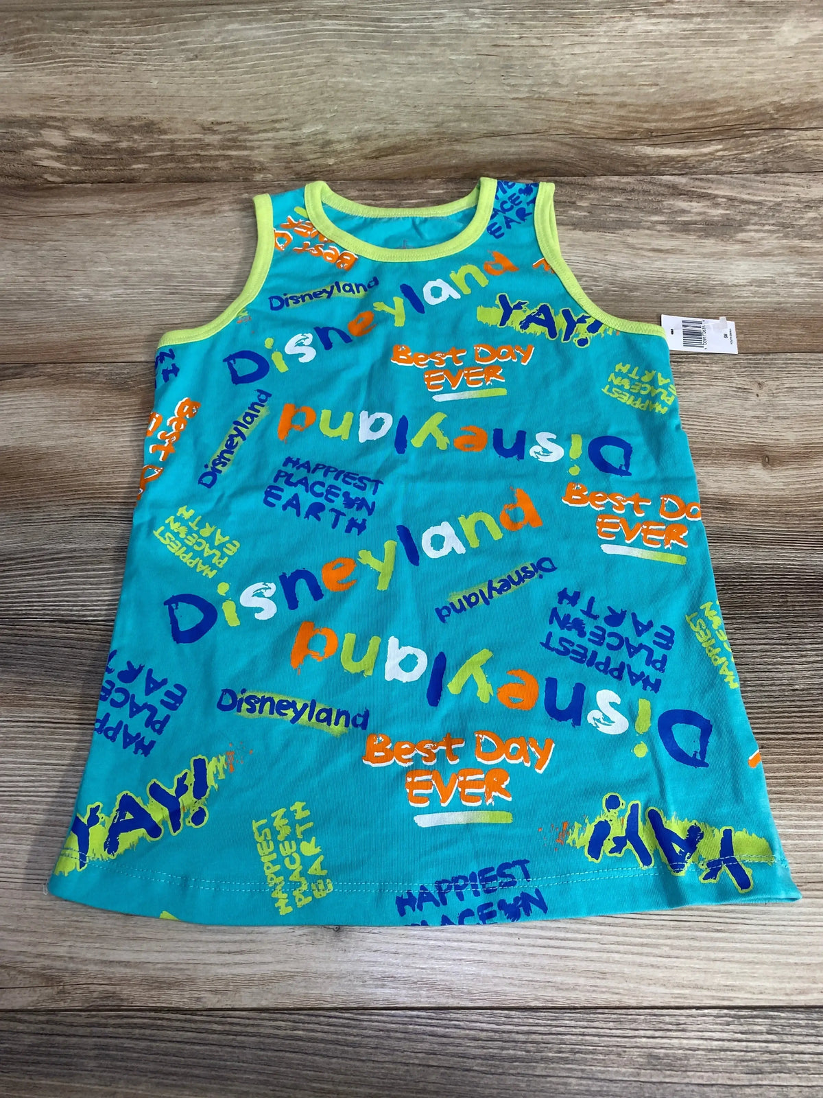 Flat-lay of teal toddler tank top with multicolor Disneyland and Best Day Ever prints and yellow trim on wood background