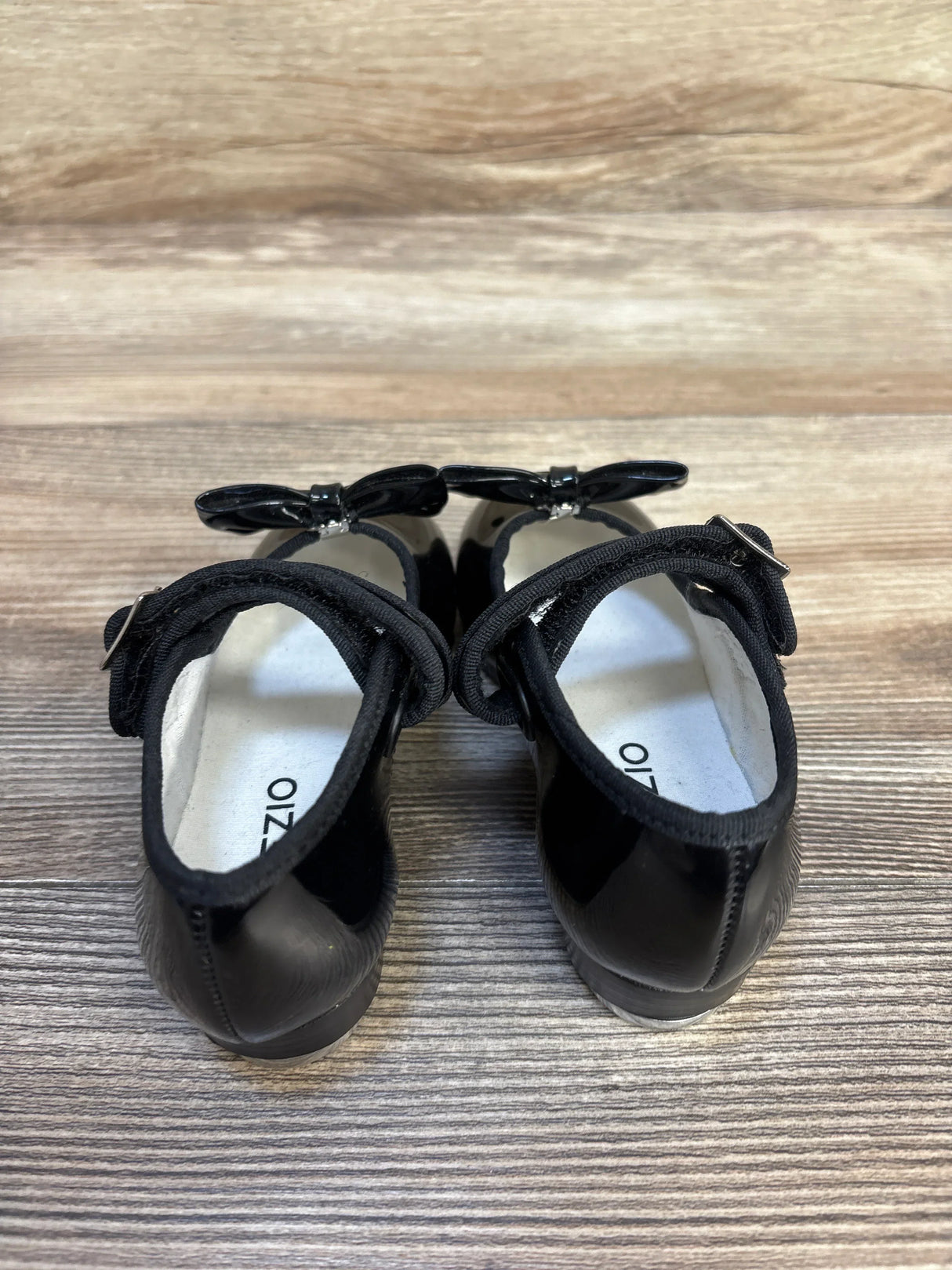 Pair of black toddler dress shoes with bows on wooden floor