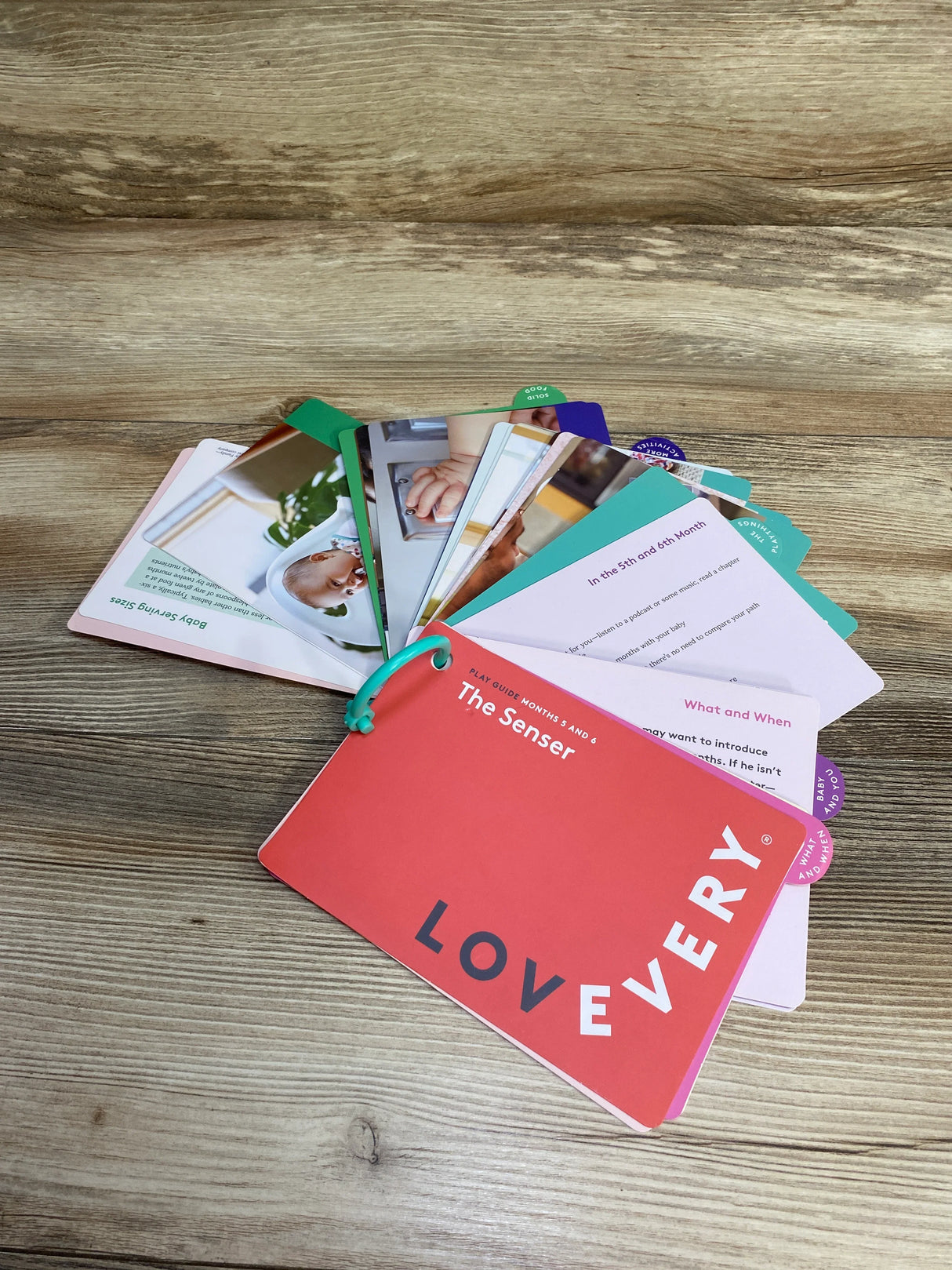 Loveyvery baby play guide cards for months 5 and 6 titled The Senser on wooden surface