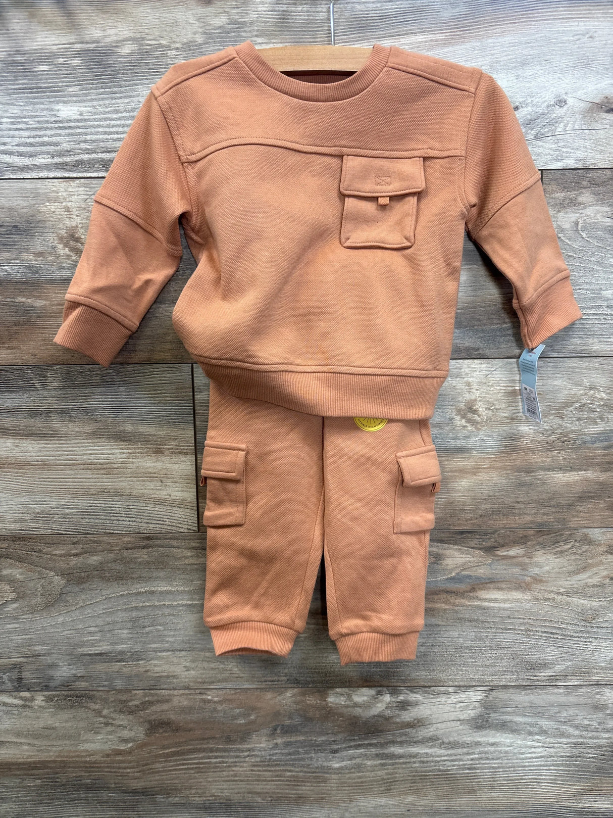 Rust orange toddler sweatshirt and jogger pants set with pockets, displayed on wooden background.