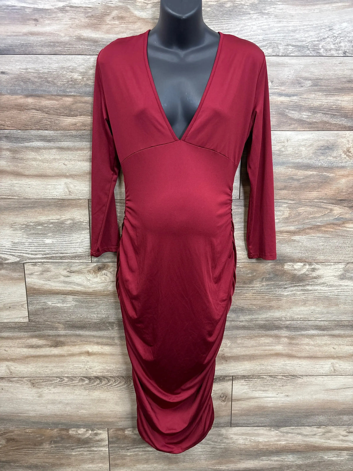 Burgundy long sleeve ruched bodycon dress with deep V-neck on mannequin, wood background