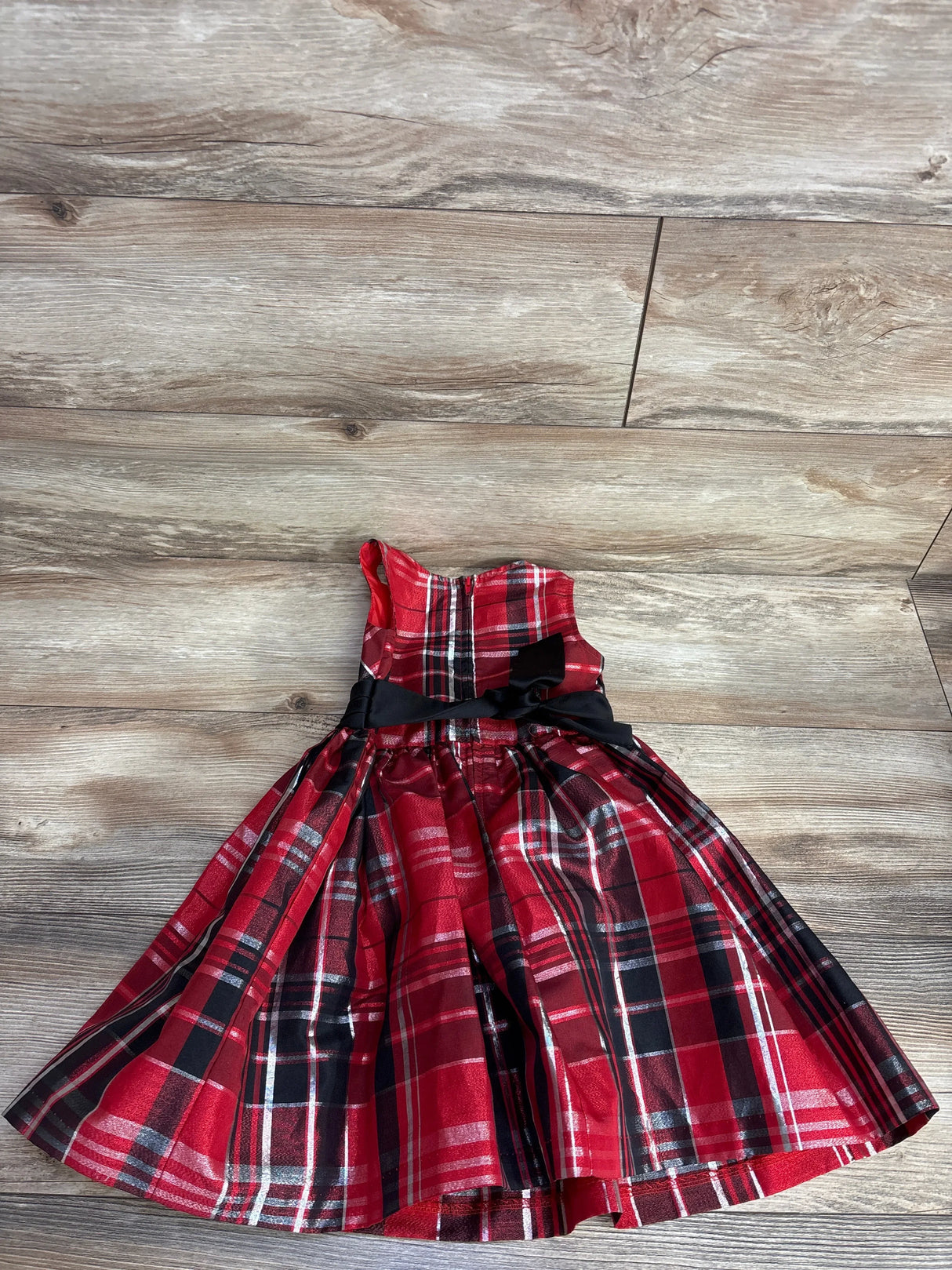 Red plaid girls holiday dress with black ribbon bow on wood floor background