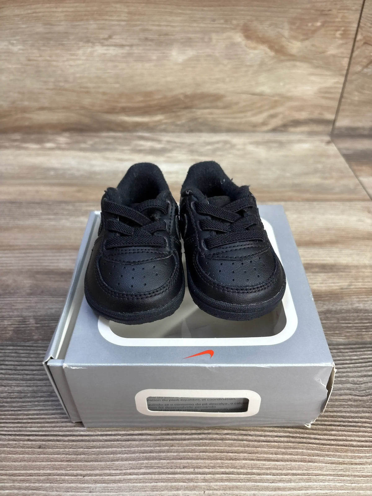Front view of Nike Air Force 1 crib shoes in black, showcasing perforated toes and laces on a Nike shoebox