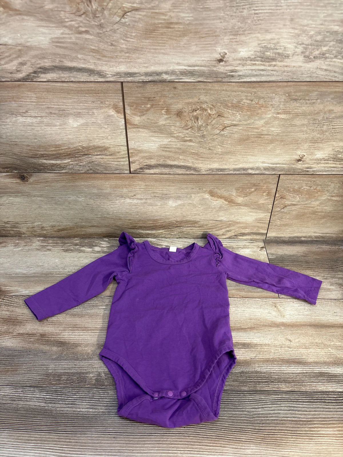Top view of purple long sleeve bodysuit for 12 to 18 months showcasing snap closure on a wood-look background