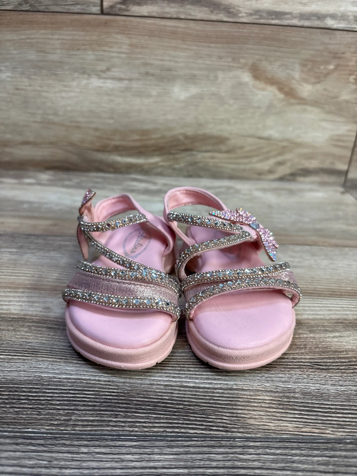 Front view of Atalina rhinestone sandals showcasing pink rhinestone straps on wood-grain flooring