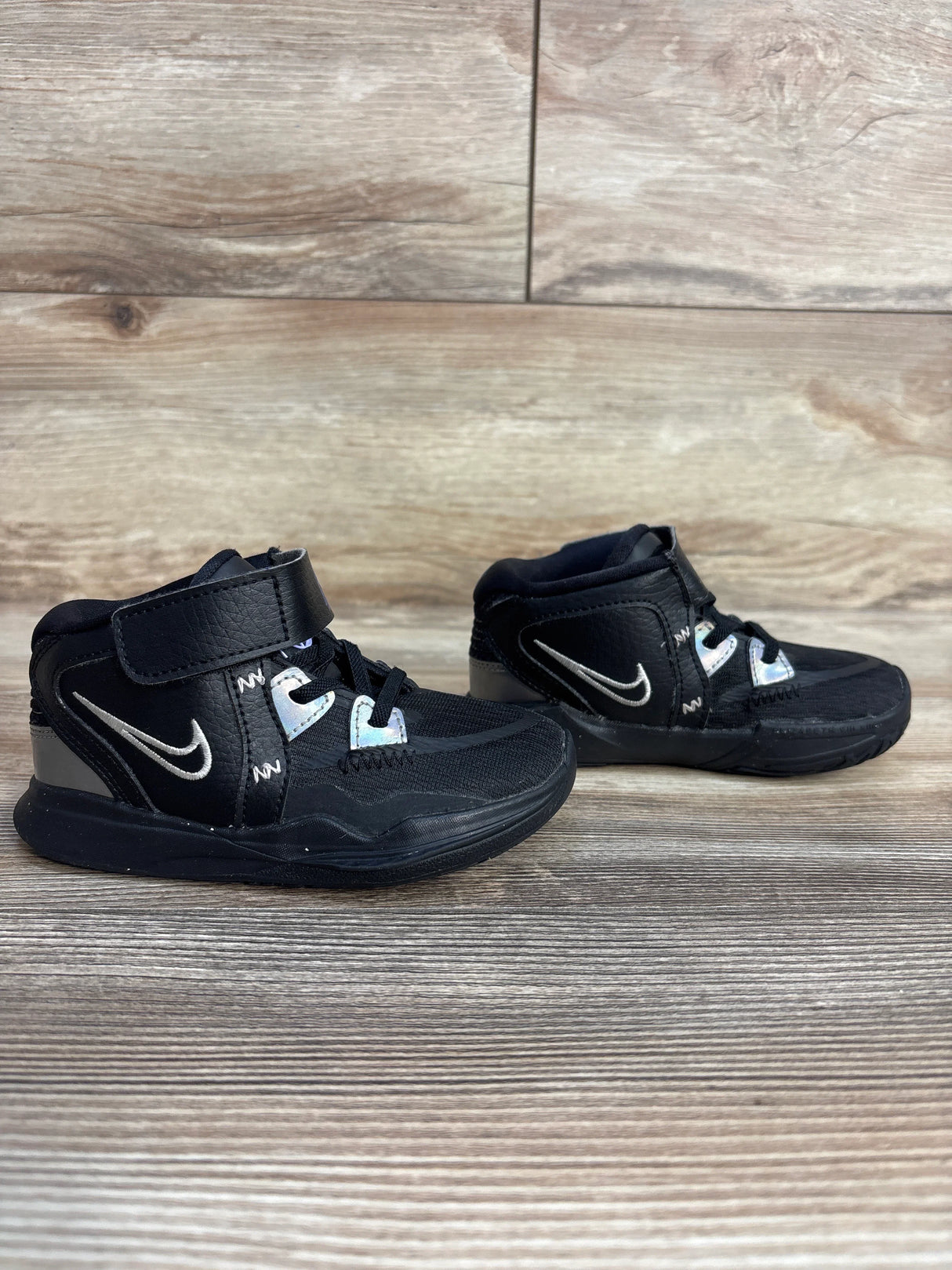 Black Nike toddler sneakers with silver swoosh logo on wood background